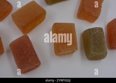 Essen, köstliche süße Gelee-Bonbons, bestreut mit Zucker, sind auf einem weißen Plastikhintergrund angeordnet. Grüne, rote, gelbe, orangene kleine Marmelade. Stockfoto