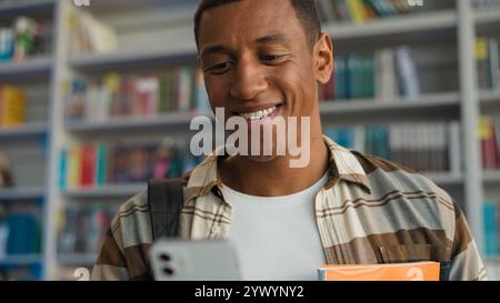Afroamerikanischer Mann, der Handy hält Smartphone lächelnde Technologie soziale Netzwerke verbinden Bibliothek Bildung Lernen Bücherei Universität College Stockfoto
