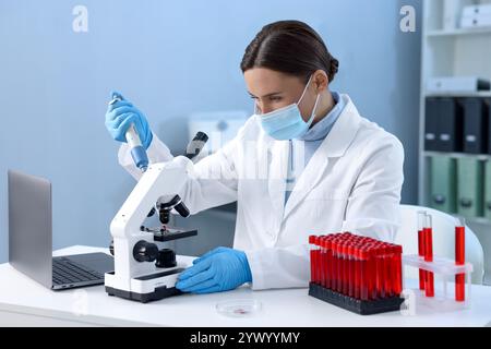 Labortests. Arzt tropft Blutprobe auf Glasträger, während er mit dem Mikroskop im Innenbereich arbeitet Stockfoto