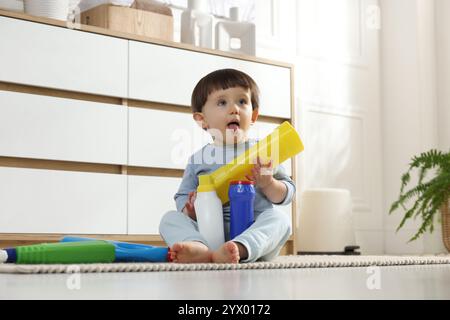 Kleiner Junge, der mit Waschmittelflaschen in der Nähe des Schranks zu Hause spielt. Kind in Gefahr Stockfoto