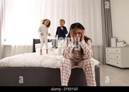 Überwältigte Mutter und ihre verspielten Kinder zu Hause im Bett Stockfoto