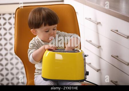 Kleiner Junge, der mit Toaster in der Küche spielt. Gefährliche Situation Stockfoto