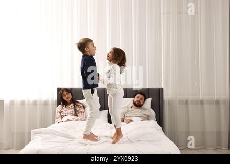 Überforderte Eltern und ihre verspielten Kinder zu Hause im Bett Stockfoto