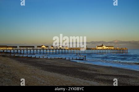 Southwold, Suffolk, England, Großbritannien - Blick entlang des Southwold Beach in Richtung Pier bei Sonnenuntergang mit Wellen, die an der Küste um den Pier brechen Stockfoto