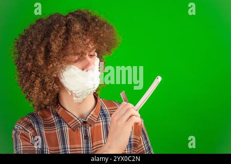 Elegant in einem formellen Hemd gekleidet, reibt der lockige Junge sanft Schaum über sein Gesicht, während der leuchtend grüne Chroma-Schlüssel die Sauberkeit und die Sauberkeit verbessert Stockfoto