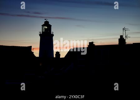 Southwold, Suffolk, England, Großbritannien - Silhouette des Leuchtturms Southwold bei Sonnenuntergang. Der viktorianische Leuchtturm befindet sich im Stadtzentrum, umgeben von Hütten Stockfoto