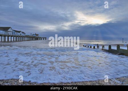 Southwold, Suffolk, England, Großbritannien - Southwold Pier bei Sonnenaufgang mit Wellen, die an der Küste um den Pier herum brechen, und Sonnenstrahlen von aufgehender Sonne Stockfoto