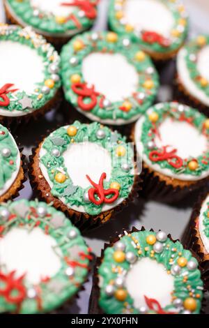 Close up-Cupcakes mit weißgoldener grüner und roter Zuckerglasur und einem weihnachtsbaum im Hintergrund Stockfoto