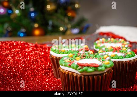 Close up-Cupcakes mit weißgoldener grüner und roter Zuckerglasur und einem weihnachtsbaum im Hintergrund Stockfoto