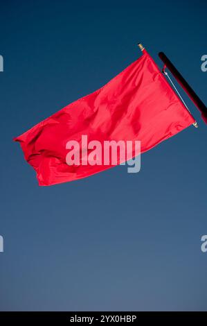 Rote Flagge, die auf dem Wind fliegt, mit blauem Himmel im Hintergrund Stockfoto