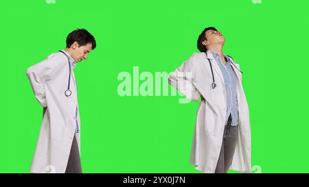 Ärztin mit akuten Schmerzen im unteren Rücken im Studio, Skoliose und Muskelbeschwerden. Der Arzt kümmert sich um Rückenschmerzen von Burnout, Greenscreen Hintergrund. Kamera B.. Stockfoto