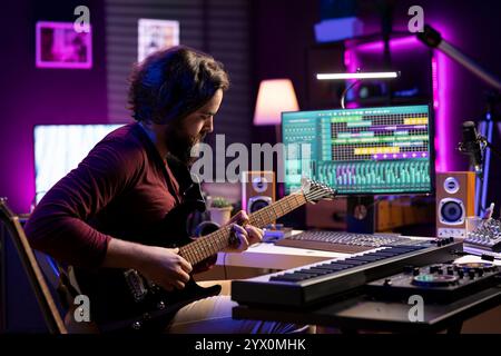 Junger Künstler nimmt sich selbst beim Spielen der Akustikgitarre im Heimstudio auf, erstellt neue Streicherakkorde und bearbeitet sie mit der daw-Software. Musiker, der neue Soundtracks mit Instrument und Verstärker produziert. Stockfoto