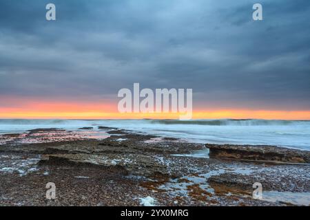 Meereslandschaft am Strand Ericeira,. Explosiver Sonnenuntergang in intensiver Farbfotografie. Ebbe und der Schaum zwischen den Felsen Portugal Meereslandschaft. Li Stockfoto