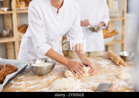 Hände eines professionellen Bäckers, der Teig auf mehlem Tisch kntet Stockfoto