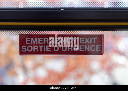 Nahaufnahme eines „Notausgangs. Sortie D'Urgence'-Aufkleber auf einem Busfenster, der Sicherheit und zweisprachige Beschilderung hervorhebt. Stockfoto