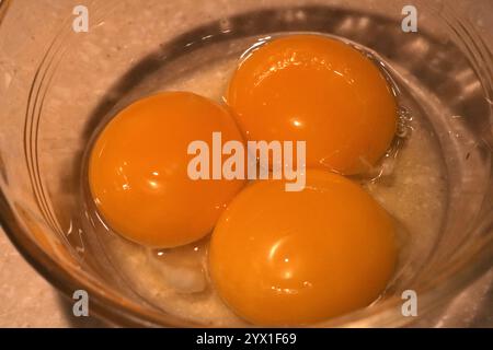 Drei frische Eigelbe in einer transparenten Glasschale auf einer hellen Oberfläche Stockfoto