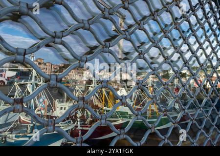 Eine Schaufensterscheibe mit Fensterläden und Modellen von Fischerbooten spiegelt die Hafenfront des Dorfes in Saint-Jean-de-Luz, Frankreich, wider. Das Dorf fällt entlang der t Stockfoto