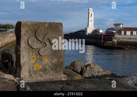 Ein Steinmarker mit einem Lauburu, dem traditionellen Symbol des Baskenlandes, entlang des Nivelle-Flusses in Saint-Jean-de-Luz, Frankreich. Das Dorf fällt A Stockfoto