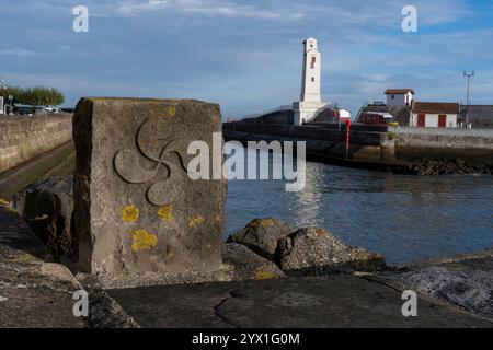 Ein Steinmarker mit einem Lauburu, dem traditionellen Symbol des Baskenlandes, entlang des Nivelle-Flusses in Saint-Jean-de-Luz, Frankreich. Das Dorf fällt A Stockfoto