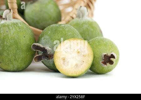 Eine Nahaufnahme frischer Feijoa-Früchte, die aus einem Korb auf eine weiße Oberfläche geschüttet werden. Das Bild hebt die leuchtende grüne Farbe und die natürliche Textur hervor Stockfoto