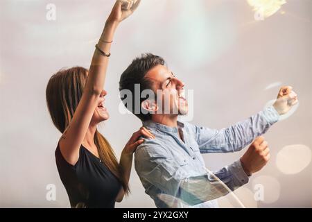 Ein junges Paar feiert gemeinsam, hebt die Arme in freudigem Triumph, strahlt Aufregung und Begeisterung aus und teilt einen Moment des reinen Glücks Stockfoto