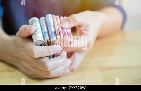 Geschäftsfrau zählt Geld. Reiche weibliche Hände halten und zählen Barscheine von thailändischen Scheinen oder Banknoten auf Holztisch. Selektiver Fokus. Stockfoto