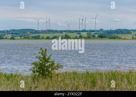 Ein Blick auf Windmühlen, die Strom aus erneuerbaren Energiequellen erzeugen, auf einem kleinen Hügel hinter einem bezaubernden See. Stockfoto