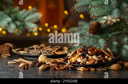 Weihnachtliche Gewürze, verschiedene Nüsse, Rosinen und trockene Zitrusscheiben auf einem Küchentisch. Weihnachtliches Stillleben mit Fichtenzweigen und getrockneten Früchten. Im Stockfoto