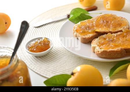 Küchenbank mit Frühstück, zubereitet mit Pflaumenmarmelade auf Toast auf Teller und Gläsern und Obst herum. Erhöhte Aussicht. Stockfoto