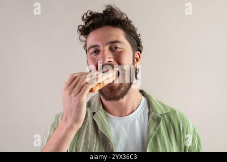 Junger Mann mit lockigen Haaren, der ein Sandwich isst, ehrlicher Lebensstil - schöner Kerl, der einen Snack beißt. Stockfoto