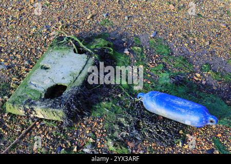 Ein Betonblock an einem Strand mit einem blauen Schwimmer, der mit einem Seil befestigt ist, der Block umhüllt von Algen und Algen. Stockfoto