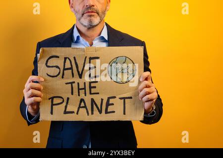 Ein Mann in einem Anzug, der ein Schild mit der Aufschrift "RETTET DEN PLANETEN" zeigt. Stockfoto