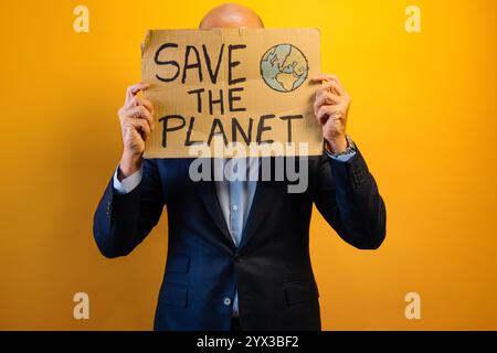 Ein Mann in einem Anzug, der ein Schild mit der Aufschrift "RETTET DEN PLANETEN" zeigt. Stockfoto