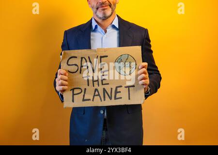 Ein Mann in einem Anzug, der ein Schild mit der Aufschrift "RETTET DEN PLANETEN" zeigt. Stockfoto