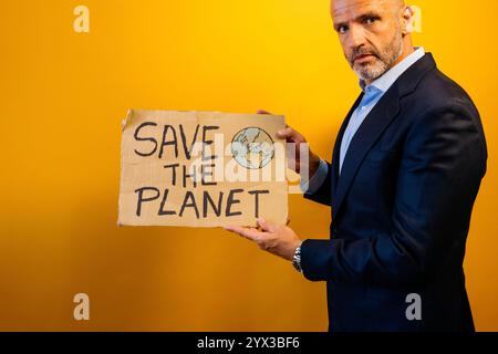 Ein Mann in einem Anzug, der ein Schild mit der Aufschrift "RETTET DEN PLANETEN" zeigt. Stockfoto