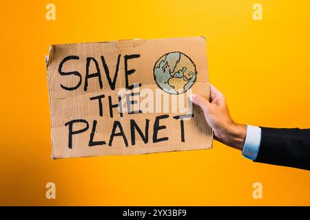 Ein Mann in einem Anzug, der ein Schild mit der Aufschrift "RETTET DEN PLANETEN" zeigt. Stockfoto