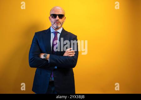 Ein Mann in Anzug und Sonnenbrille steht vor einer gelben Wand. Stockfoto