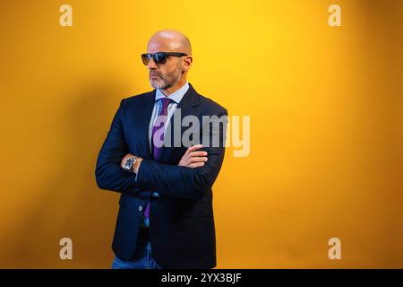 Ein Mann in Anzug und Sonnenbrille steht vor einer gelben Wand. Stockfoto