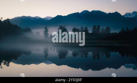 Reflexionen im Lake Matheson bei Sonnenaufgang im Nebel, Mount Cook National Park Mountains im Hintergrund bei Sonnenaufgang im Nebel - Westküste, Neuseeland Stockfoto