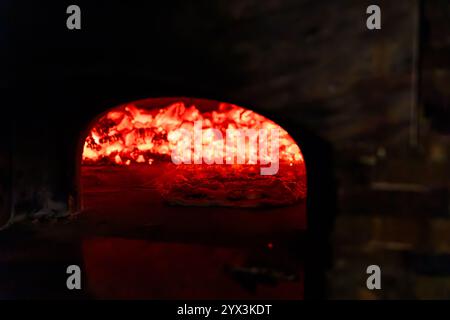 Eine Pizza, die in einem glühenden Holzofen mit intensiver Glut gebacken wird Stockfoto