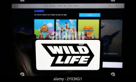 In dieser Fotoabbildung hält eine Person ein Handy mit dem Logo des brasilianischen Spieleunternehmens Wild Life Inc. (Wildlife Studios) vor der Webseite. Stockfoto