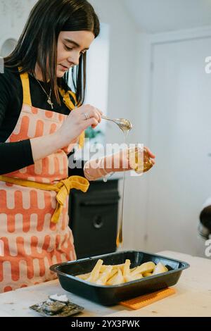 Eine Frau macht Honig auf einer Küchenzeile. Sie trägt eine Schürze und eine Halskette Stockfoto