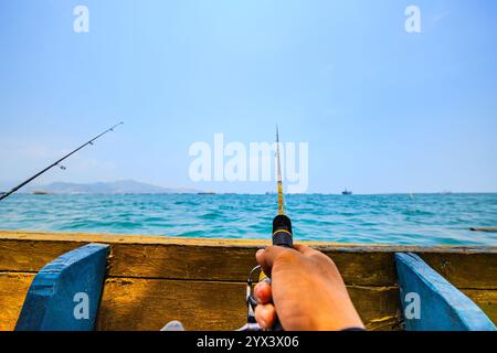 Die Hand des Mannes greift eine Angelrute während einer Küstenexpedition. Mann fischt in einem traditionellen Boot inmitten der Wellen des Blauen Ozeans. Stockfoto