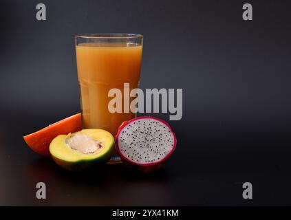 Eine Mischung aus frisch gepressten Säften aus tropischen Früchten auf schwarzem Hintergrund, neben den Hälften reifer Grapefruit, Mango und pitaya. Nahaufnahme. Stockfoto