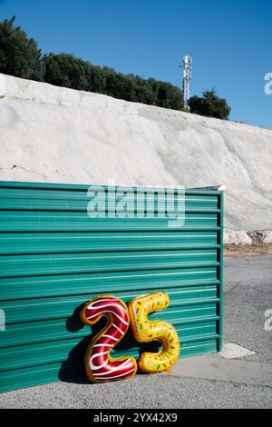 Zwei Folienballons in verschiedenen Farben und Mustern, die die Zahl 25 bilden, die auf einer grünen gewellten Metallwand befestigt sind Stockfoto