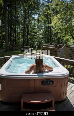 Eine Frau wird von hinten gesehen, die sich in einem luxuriösen Whirlpool im Herzen des Waldes in Slade, Kentucky, befindet. Umgeben von üppigem Grün und dem Stockfoto