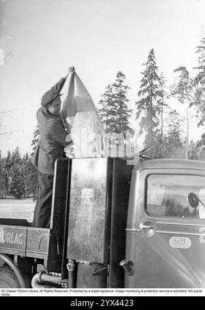 Holzgas 1942. Ein Mann füllt mehr Kohle in den Behälter, um die Holzgasanlage zu betanken. Ein natürliches Merkmal während dieser Jahre während des Zweiten Weltkriegs war die Wood-Vergasungseinheit auf Autos und Lkws. Holzgas ist ein Gas, das bei der unvollständigen Verbrennung von Holz oder Kohle entsteht und zum Antrieb von Fahrzeugen verwendet wurde. Der Fahrer musste die Kohle selbst auffüllen und sicherstellen, dass die Verbrennung ordnungsgemäß funktioniert. Aufgrund des Treibstoffmangels während des Zweiten Weltkriegs spielte Holzgas eine wichtige Rolle für den Fortbestand des Transports. Stockfoto