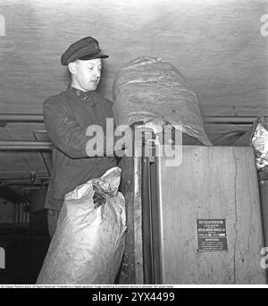 Holzgas 1942. Ein Mann füllt mehr Kohle in den Container, um die Holzgaseinheit seines LKW zu betanken. Ein natürliches Merkmal während dieser Jahre während des Zweiten Weltkriegs war die Wood-Vergasungseinheit auf Autos und Lkws. Holzgas ist ein Gas, das bei der unvollständigen Verbrennung von Holz oder Kohle entsteht und zum Antrieb von Fahrzeugen verwendet wurde. Der Fahrer musste die Kohle selbst auffüllen und sicherstellen, dass die Verbrennung ordnungsgemäß funktioniert. Aufgrund des Treibstoffmangels während des Zweiten Weltkriegs spielte Holzgas eine wichtige Rolle für den Fortbestand des Transports. Kristoffersson Ref. A125-3 Stockfoto