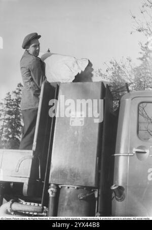 Holzgas 1942. Ein Mann füllt mehr Kohle in den Behälter, um die Holzgasanlage zu betanken. Ein natürliches Merkmal während dieser Jahre während des Zweiten Weltkriegs war die Wood-Vergasungseinheit auf Autos und Lkws. Holzgas ist ein Gas, das bei der unvollständigen Verbrennung von Holz oder Kohle entsteht und zum Antrieb von Fahrzeugen verwendet wurde. Der Fahrer musste die Kohle selbst auffüllen und sicherstellen, dass die Verbrennung ordnungsgemäß funktioniert. Aufgrund des Treibstoffmangels während des Zweiten Weltkriegs spielte Holzgas eine wichtige Rolle für den Fortbestand des Transports. Stockfoto