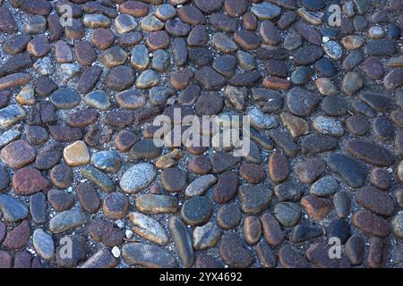 Runde Steine im Boden. Die Textur der Pflastersteine auf der Straße. Asphaltierte Straße für Fußgänger. Die Pflastersteine. Hintergrund Stockfoto